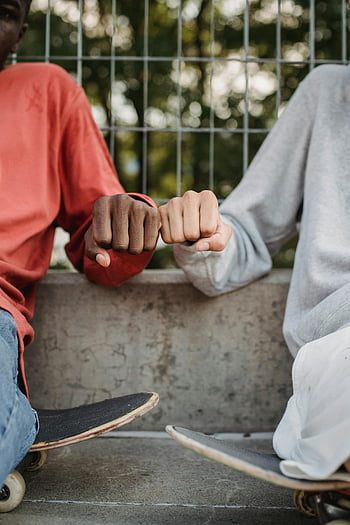Vrienden stoten vuisten, Twee tieners, vuist hobbel, skateboards, buitenshuis, zittend, toevallig, vriendschap, stedelijke omgeving, jeugd Cultuur, skateboarden