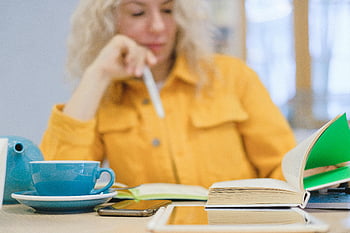 female student, homework assignment, studying, coffee, books, tablet, cozy indoor setting, woman, yellow jacket, pen, books and coffee