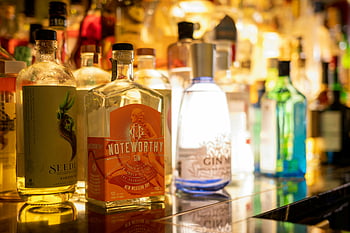 alcohol bottles, gin bottles, polished bar counter, warm lighting, vibrant display, various gin, bar counter, alcohol display, gin display, bar scene, warm ambiance