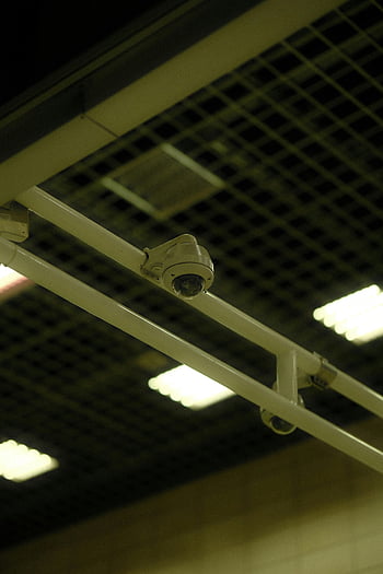 ceiling-mounted security camera, indoor setting, close-up, grid, lights, indoor environment, security camera, ceiling-mounted, indoor security, grid ceiling, fluorescent lights