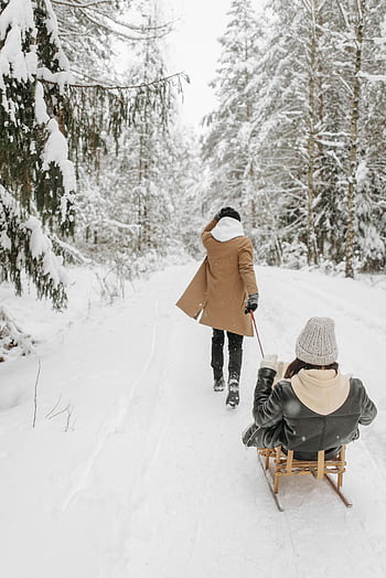 winter sledding, snow-covered forest, couple sledding, winter fun, togetherness, man pulling sleigh, woman on sleigh, snowy landscape, outdoor winter activities, winter recreation, winter scenery