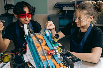 red protective goggles, black shirt, robotics project, tech lab, machinery details, students collaborating, project development, engineering, technical skills, teamwork, laboratory equipment