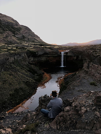 Uomo seduto vicino alle cascate, Viaggiatore solitario, paesaggio drammatico, cascata, scenario naturale, avventura all'aria aperta, vista panoramica, terreno roccioso, Zona montuosa, ambiente sereno, fotografia di viaggio