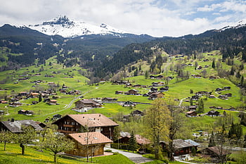 hnědý dům, modré nebe, okouzlující vesnice, svěží zelené kopce, zasněžené hory, interlaken, švýcarsko, fotografování, scénické krajiny, alpské vesnice, venkovské scenérie