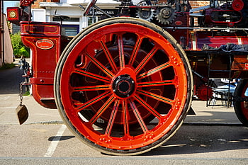 red metal carriage wheel, vintage steam engine, red and black colors, outdoor display, detailed view, steam engine wheel, red carriage wheel, vintage wheel, outdoor steam engine, red and black wheel, steam engine parts