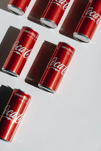 COCA-COLA CANS, bílý stůl, živé uspořádání, Kultovní Coca-Cola, Červené plechovky, bílé pozadí, Obsazení stínů, Originální chuť, plechovky od limonády, minimalistický design, produktová fotografie