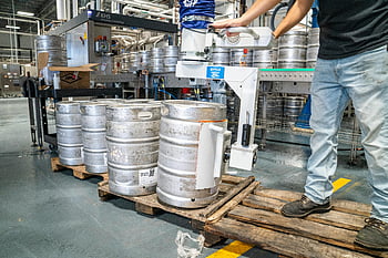 man operating machinery, silver steel kegs, brewery warehouse, worker, stacking kegs, industrial equipment, keg handling, brewery operations, steel kegs, pallet, machinery operation