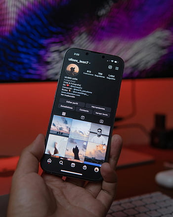 smartphone, social media profile, close-up, indoor setting, warm lighting, hand holding phone, digital display, user interface, mobile device, profile page, social networking