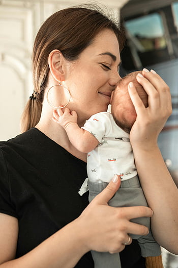 Mutter küsst Baby, zärtlicher Moment, liebevolle Umarmung, Neugeborenes, Innenfoto, Mutterschaft, Familienbund, Emotionale Verbindung, Mutter und Kind, Säuglingspflege, liebevolle Mutter