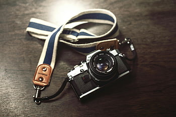 Olympus analog camera, vintage photography, black and gray bridge camera, white and blue lanyard, classic camera, wooden table, strap, retro charm, analog photography, vintage camera, Olympus camera