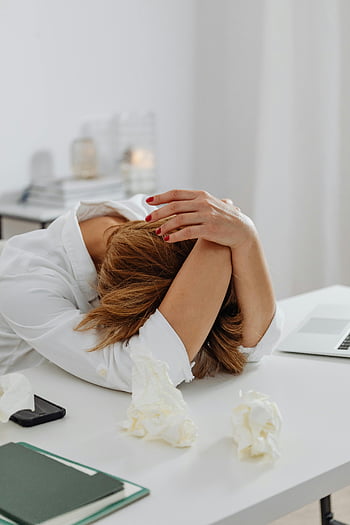stressed woman, white table, distress, head in hands, tissue papers, desk, emotional stress, office setting, work stress, mental health, fatigue