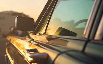 closed black vehicle door, car side window, mirror reflection, sunset light, warm moment, peaceful scene, close-up photo, vehicle exterior, side mirror, car door handle, golden hour lighting