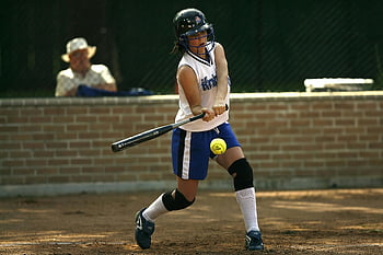 female athlete, white sleeveless jersey, black baseball bat, green tennis ball, softball game, outdoor sports, batting stance, concentration, knee brace, sports action, female softball player