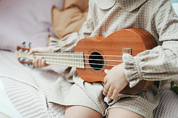 μικρό παιδί παίζοντας ukulele, Παιδικό χτύπημα ukulele, εσωτερική μουσική στιγμή, ξύλινη ukulele, γαλήνια μουσική, μικρός μουσικός, παιχνίδι σε εσωτερικό χώρο, νέος μουσικός, ukulele παίκτης, παιδικό παίζοντας μουσική, παίζοντας εσωτερικά ukulele