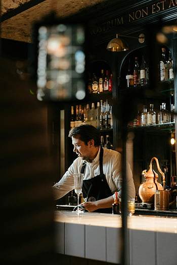 barista qualificato, Miscelazione del cocktail, bar elegante, competenza in mixologia, camicia bianca, bancone da bar, bottiglie di liquore, Setup a barre, barista professionista, Atmosfera da bar, preparazione di bevande