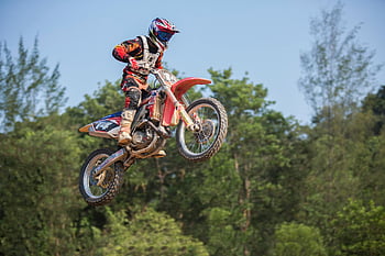 man riding dirt motorcycle, motocross rider, aerial stunt, vibrant forest, daylight, motocross, dirt bike, outdoor sports, action sports, motorcycle jump, forest backdrop