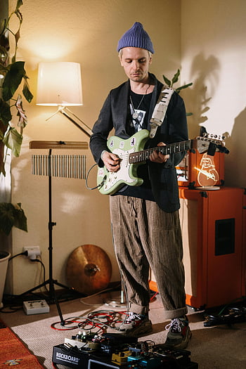 man in black suit jacket, playing white electric guitar, cozy home studio, musician playing guitar, effects pedals, indoor music session, electric guitar player, home recording setup, music studio equipment, casual music performance, indoor guitar playing