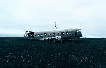 abandoned plane wreck, Icelandic beach, eerie scene, person standing, plane wreck, Iceland, beach scene, abandoned aircraft, wrecked plane, eerie atmosphere, person on plane
