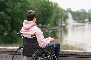 man in pink hoodie, black wheelchair, tranquil park lake, peaceful view, calm day, young man, wheelchair user, park scenery, outdoor setting, fountain background, serene environment