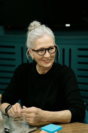 starší žena, šedé vlasy, brýle, pracovní schůzka, uvnitř, Černá košile s dlouhým rukávem, usmívající se žena, Profesionální nastavení, Kancelářské prostředí, Zralý profesionál, příležitostný obchodní oděv
