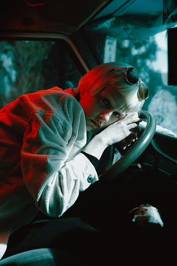 woman in car, blonde woman, white jacket, vintage car, colored lighting, artful pose, car interior, red lighting, blue lighting, sunglasses, artistic photography