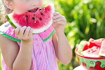 girl eating watermelon, sliced watermelon fruit, sunny outdoor setting, summer refreshment, young girl, juicy watermelon slice, beside table, outdoor photo, watermelon season, healthy snack, summer activity