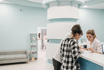 medical center reception, couple looking at documents, modern clinic reception desk, healthcare professionals assisting, medical center interior, clinic reception area, medical documents, healthcare facility, modern medical center, clinic receptionist, patient consultation