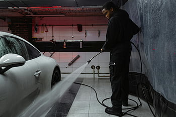 African American man, cleaning car, white car, pressure hose, indoor garage, car wash, black jacket, garage setting, car maintenance, vehicle cleaning, African American worker
