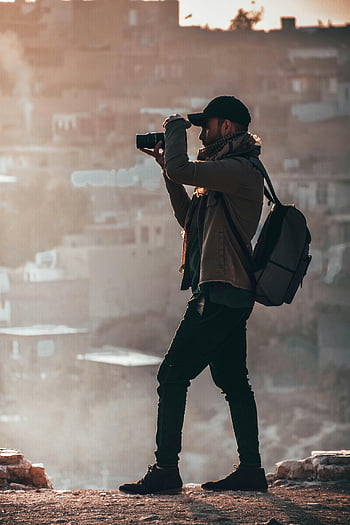 człowiek trzyma aparat, czarny aparat dslr, widok miasta, zachód słońca, Fotograf w kurtce, fotografia plenerowa, fotografia podróżnicza, Miejski krajobraz, Człowiek z plecakiem, piękny widok, fotograf podróży