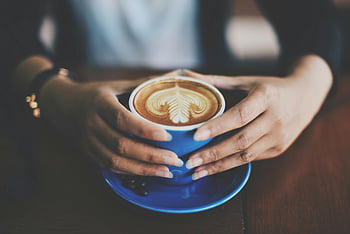 coffee cup, latte art, blue ceramic mug, hands holding, wooden table, close-up shot, intricate latte art, person holding, blue mug, coffee art, ceramic mug
