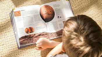 読んでいる少年、 火星に関する本、 宇宙を探検する子供、 日当たりの良いカーペット敷きの床、 宇宙の知識、 教育本、 若い読者、 火星の本、 屋内読書、 子供の勉強、 天文学の本
