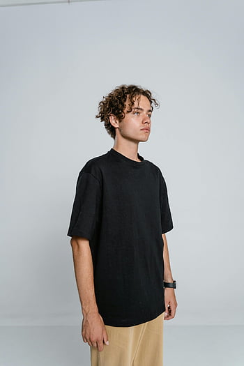 black crew neck t-shirt, teenage boy, curly hair, black t-shirt, tan pants, indoors, casual outfit, young man, simple background, studio shot, fashion style