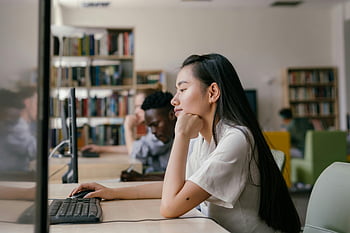 Asian student, using computer, library setting, studying diligently, university library, vibrant library, computer work, focused student, academic environment, library study, Asian woman