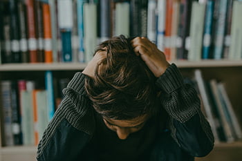 boy, long sleeves sweater, pulling hair, stressed child, frustrated child, seated in library, holding head, library setting, emotional distress, young student, academic pressure