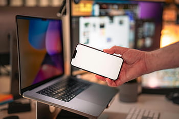 man holding smartphone, modern office, tech-oriented workspace, person with phone, laptop in background, modern workspace, smartphone in hand, tech environment, office setting, modern technology, tech-savvy workspace