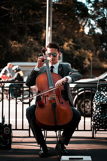 man playing cello, talented cellist, sunglasses, city street, captivating style, street performance, urban musician, classical music, outdoor concert, public performance, musical talent