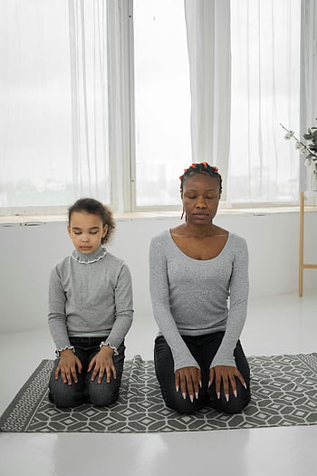 schwarze Mutter, Tochter, meditieren, geschlossene Augen, Zuhause, friedlicher Moment, Achtsamkeit, Verbindung, drinnen, Yoga Matte, natürliches Licht