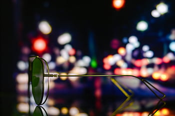 sunglasses, shallow focus, vibrant city lights, night photography, colorful urban ambiance, defocused lights, urban night scene, reflective sunglasses, night cityscape, bokeh effect, night urban lights