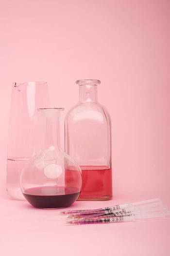 glass flasks, scientific research, various fluids, syringes, pink backdrop, lab setting, scientific works, flasks, syringes on pink, pink surface, scientific tools