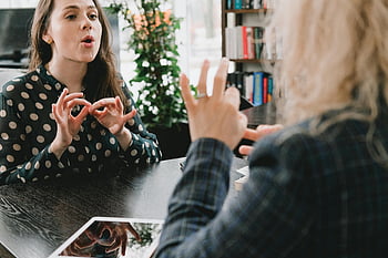sign language, young female friends, library, communication, two women, deaf community, hand gestures, indoor setting, casual conversation, educational environment, friendship