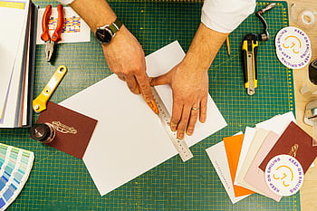 top view, person using ruler, measuring paper, grid cutting mat, designer tools, ruler, paper, cutting mat, design tools, workspace, hands