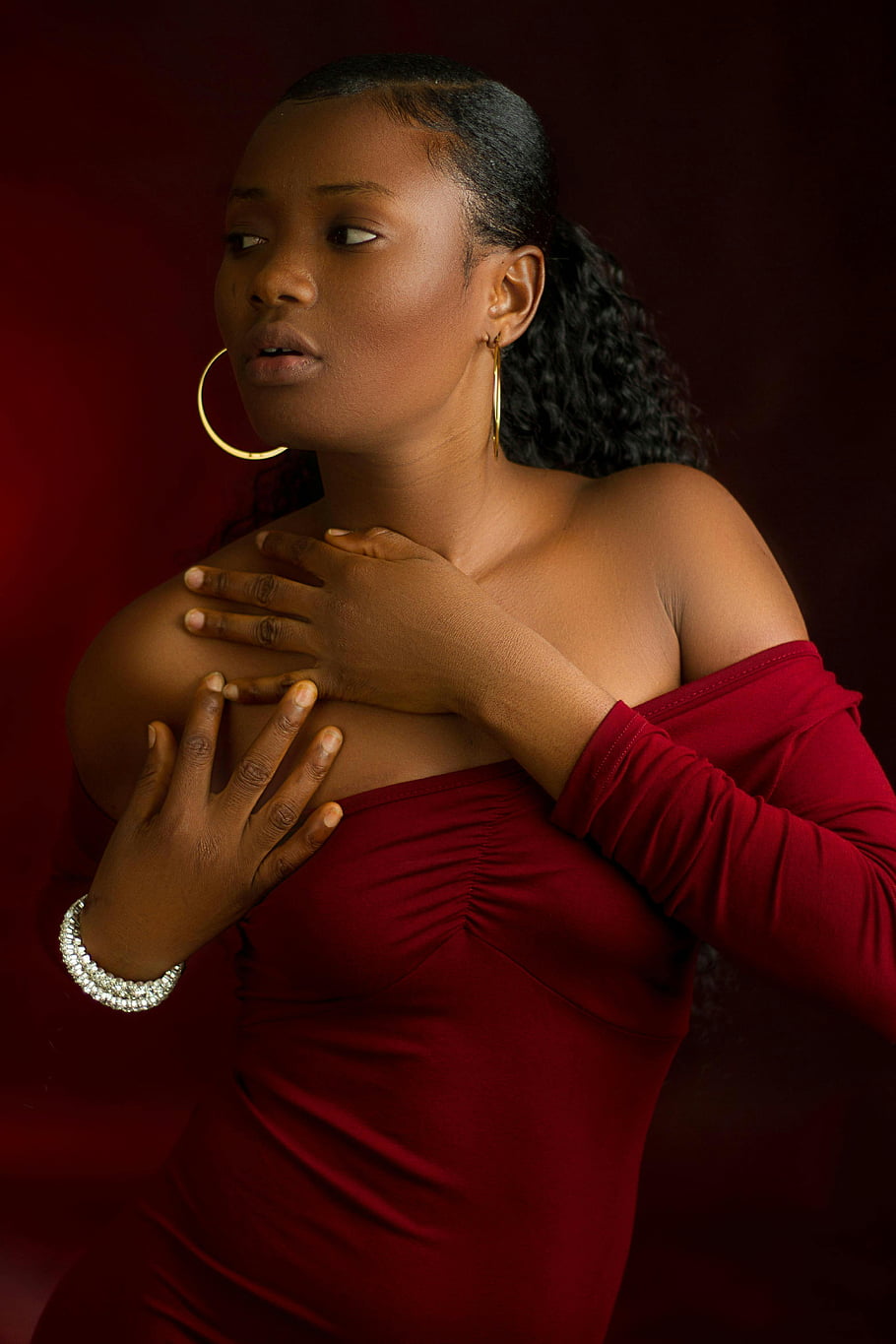 rode off-shoulder blouse, glamoureuze sieraden, opvallend portret, rode jurk, stijlvol kapsel, Gouden oorringen, elegante pose, zelfverzekerde houding, modefotografie, studio portret