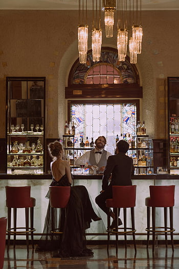 bartender serving, couple at bar, luxurious bar, elegant interior, friendly bartender, stained glass window, bar stools, elegant couple, bar counter, chandelier lighting, bar atmosphere
