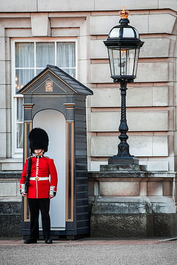 královská stráž, Buckinghamský palác, Londýn, tradiční britská kultura, ikonická scéna, červená uniforma, Černý klobouk, strážní místo, pouliční lampa, Britská monarchie, královna