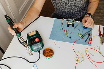 電子機器をはんだ付けする男性、 電子工作、 家庭用作業台、 はんだツール、 DIYエレクトロニクス、 クローズアップはんだ付け、 エレクトロニクスの趣味、 テーブルで作業する男性、 エレクトロニクスの修理、 家電プロジェクト、 はんだごて
