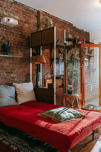 stylish bedroom, stone wall, flowerpots, rustic decor, natural lighting, loft bedroom, serene interior, red bedding, wooden furniture, brick wall, natural elements