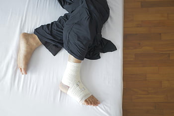 bandaged foot, injury recovery, top view, resting on bed, foot injury, bandage, recovery process, injured foot, medical bandage, bed rest, foot bandage