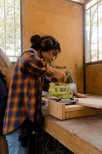 Carpenter donna, camicia a quadri, Strumento di alimentazione giallo, Strumento di alimentazione grigio, asse di legno, Workshop indoor, falegname femminile, strumento elettrico, la lavorazione del legno, carpenteria, impostazione del seminario