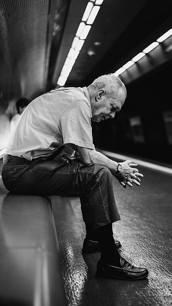 grayscale photography, sitting man, senior man, subway station, lost in thought, waiting for train, black and white, urban scene, public transportation, contemplative moment, elderly person