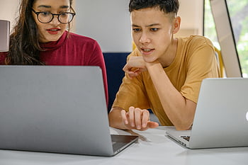 people using laptop, collaborative work session, two colleagues, indoor setting, laptops, teamwork, office environment, professional interaction, focused discussion, technology use, workplace collaboration